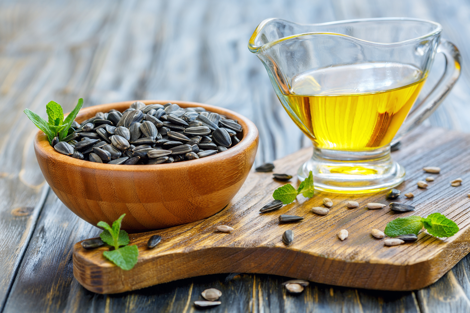 Oil and sunflower seeds in a bowl over old wooden table, selective focus.