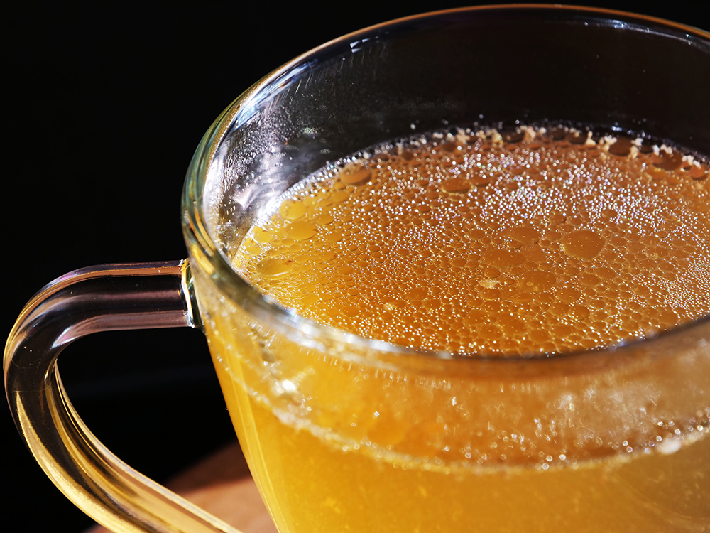 Keto bone broth in glass mug over black background. Homemade ketogenic drink, no carb, high fat superfood with essential minerals.