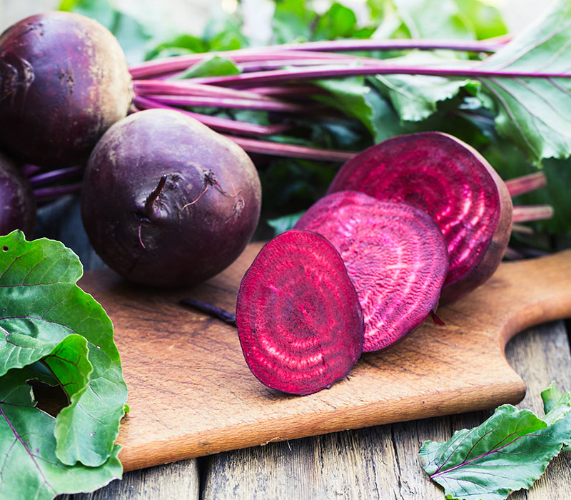 Fresh beetroots with leaves on a wooden cutting board.