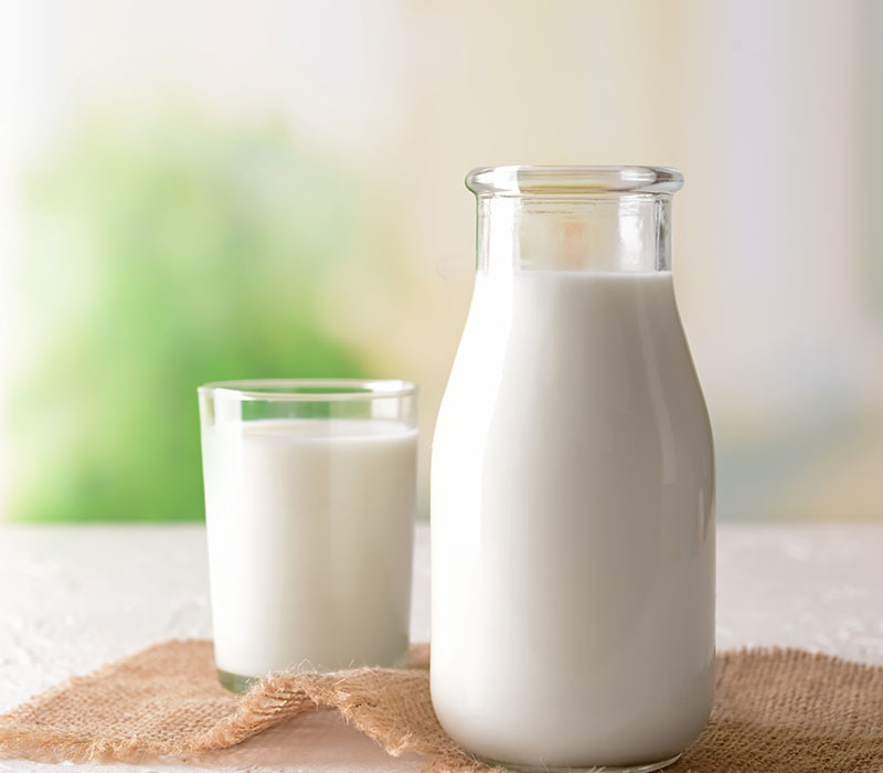 A full glass and bottle of milk on a table with a soft-focus green background.