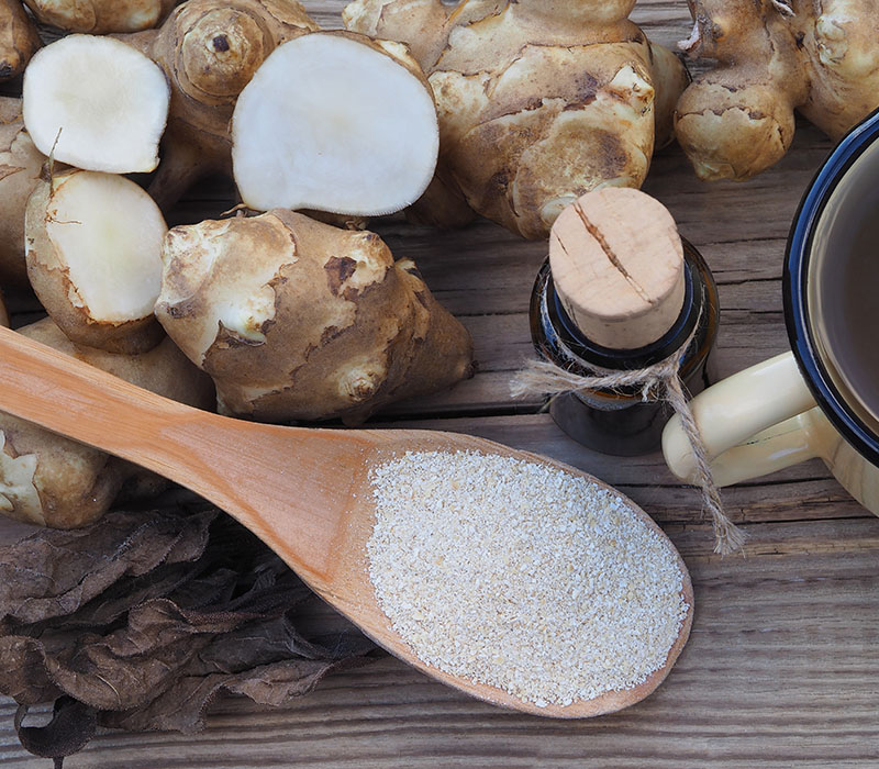 Fresh and sliced sunchoke tubers with a spoon of powder and a cup on a wooden table.