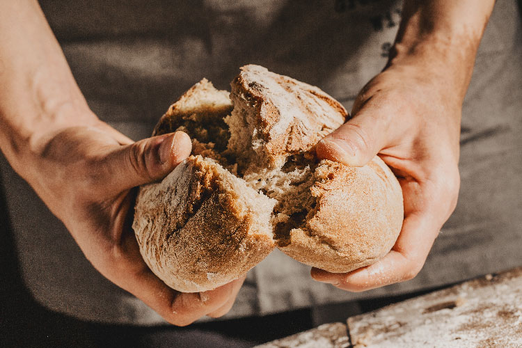 a person breaking sought dough bread in two